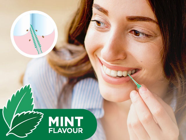 Smiling woman is cleaning between her teeth with the GUM SOFT-PICKS Minty