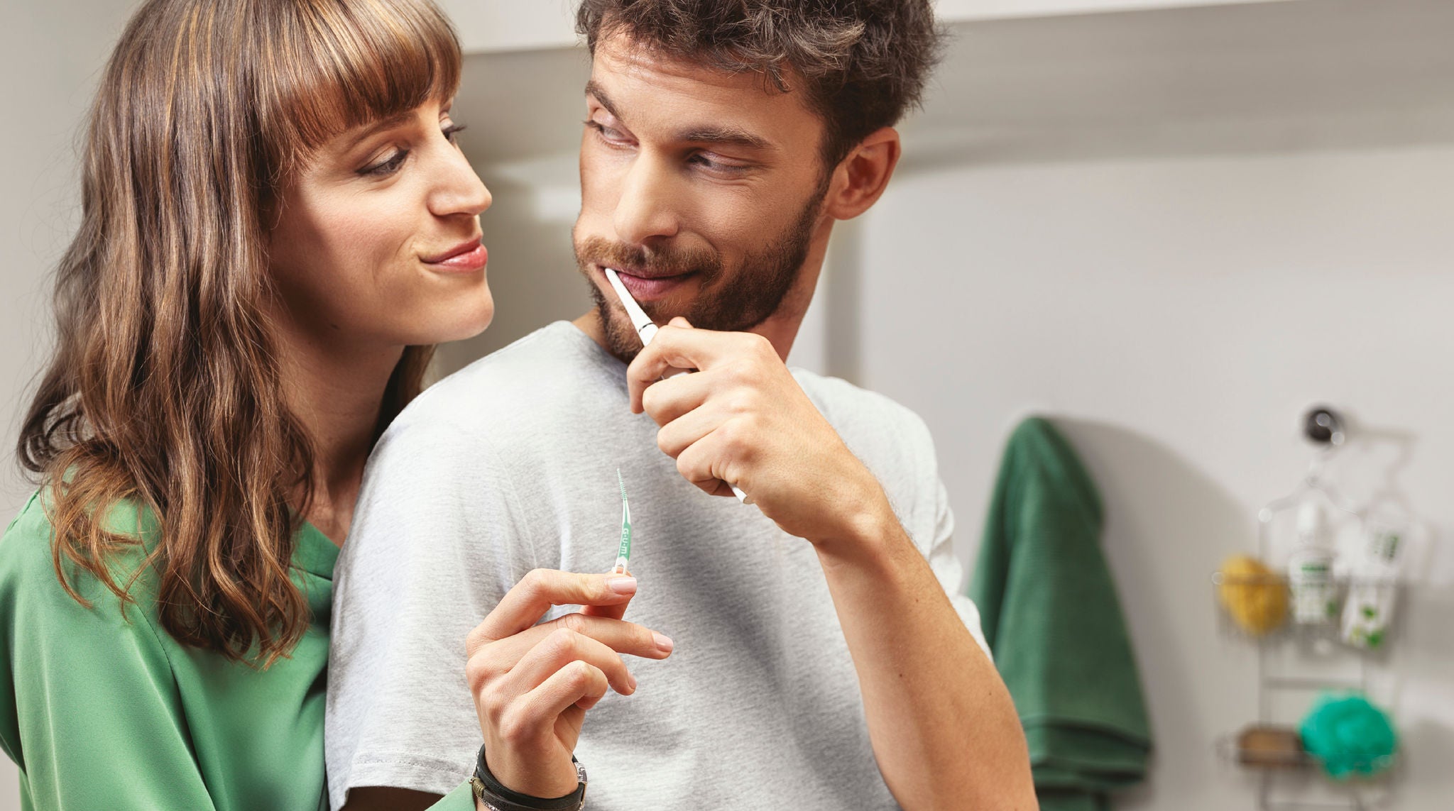 Couple souriant dans la salle de bain pour leur routine de soins bucco-dentaires, avec un bâtonnet interdentaire