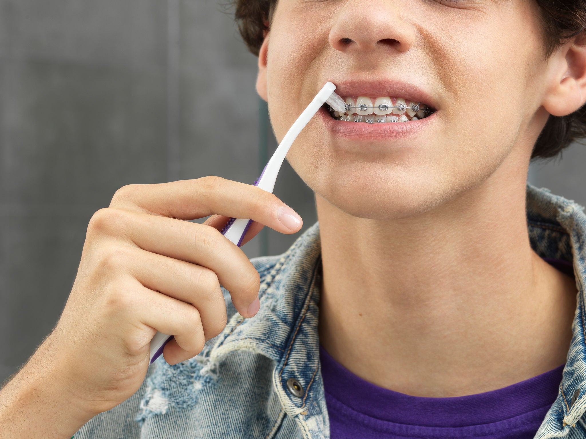 Chico joven limpiandose los dientes con braquets en el baño