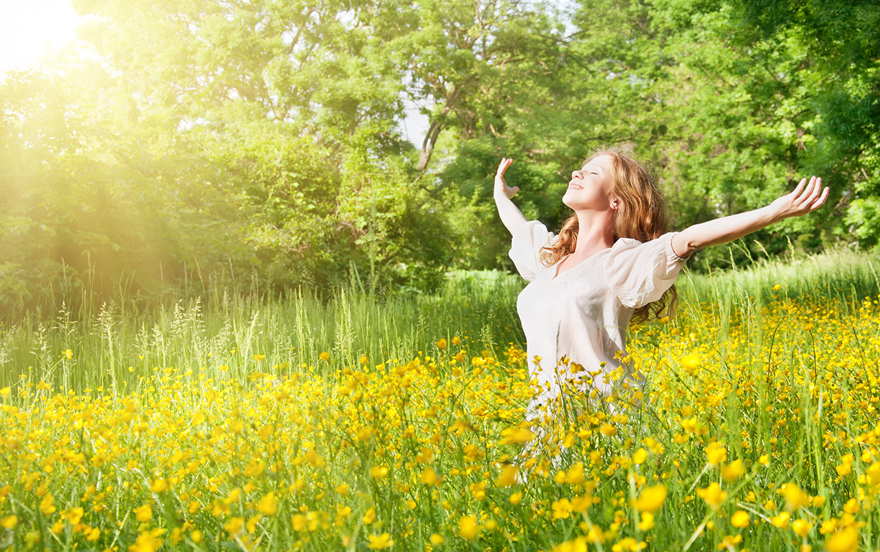 Woman outdoor in summer sun on a field of flowers green smiling