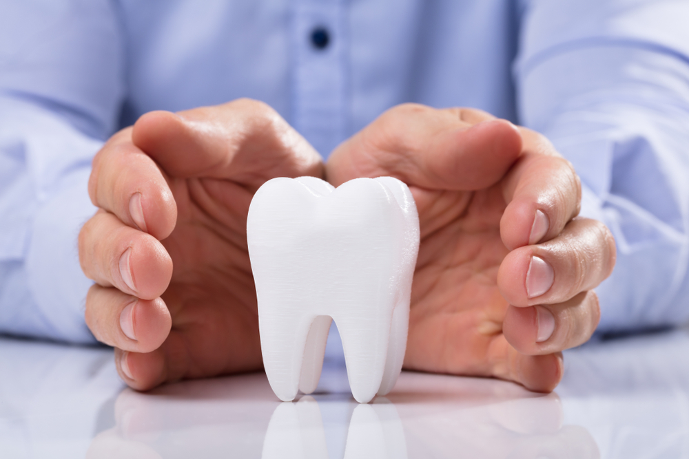 Man's Hand Protecting Healthy Hygienic White Tooth On Reflective Table