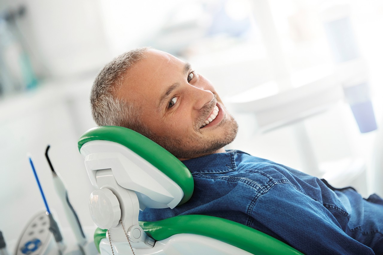 uomo sdraiato su poltrona da dentista sorride guardando verso la telecamera